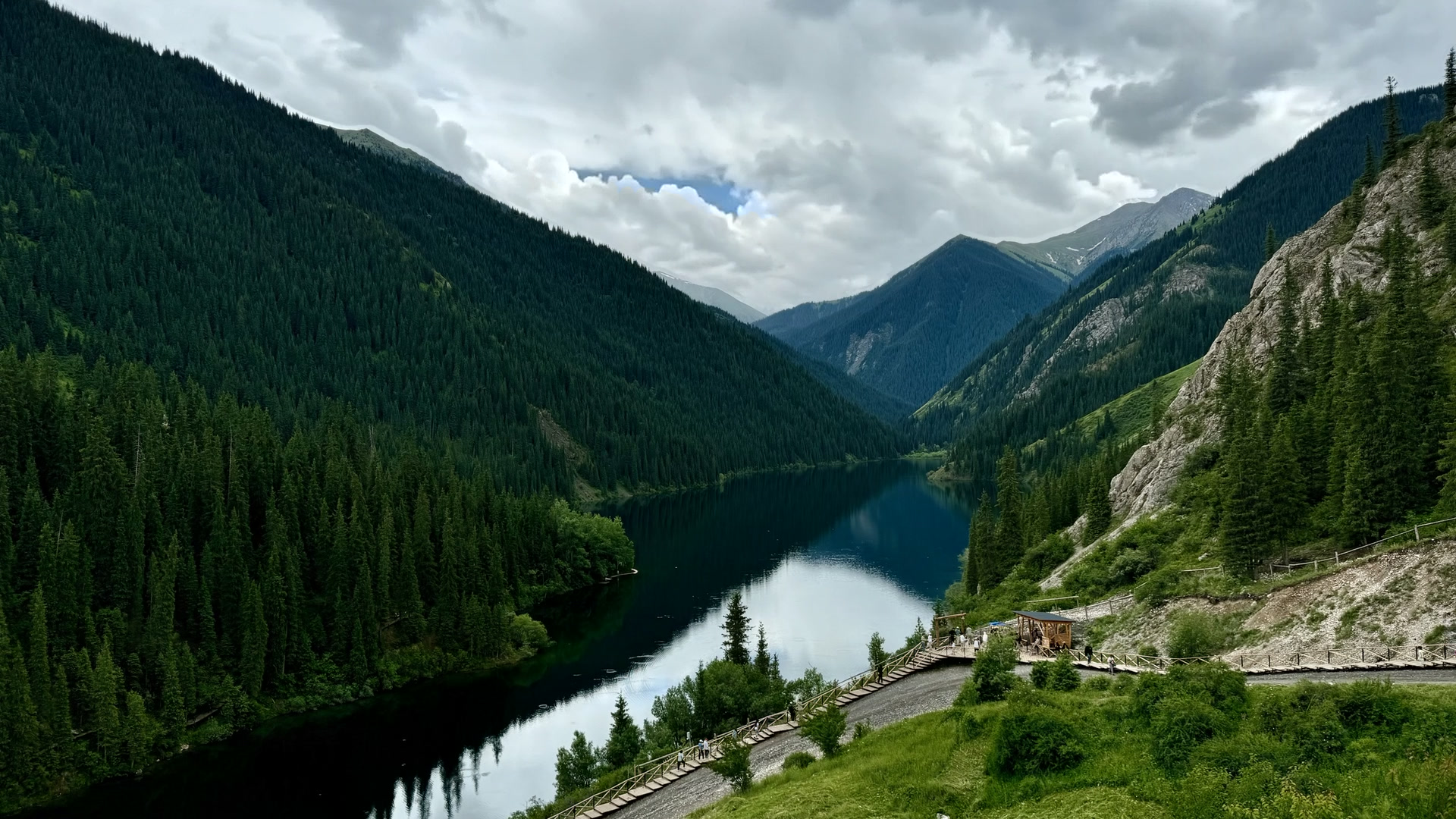 Storm light over the first Kolsai lake between spruce-covered mountain slopes