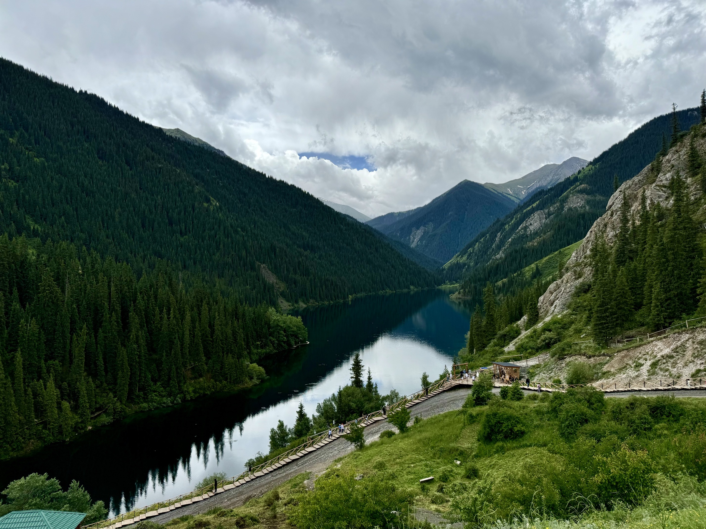 Storm light over the first Kolsai lake between spruce-covered mountain slopes